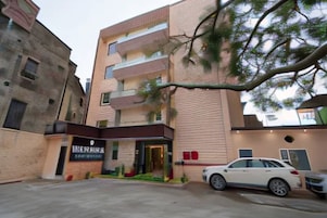 Un edificio de varios pisos con diseño moderno, que cuenta con una entrada destacada y un estacionamiento con automóviles.