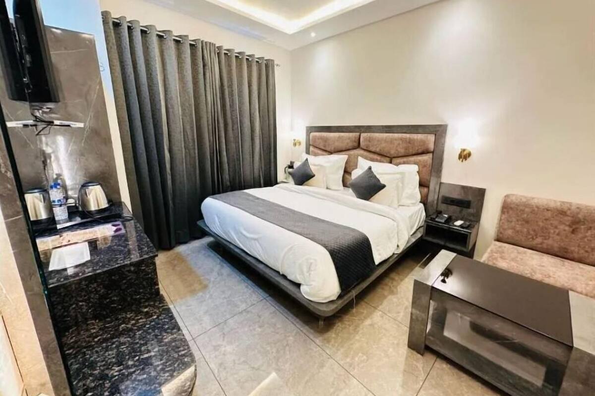 Una habitación de hotel moderna con una cama grande, un sofá, una mesa de centro, un televisor y un área de baño con ducha e inodoro.