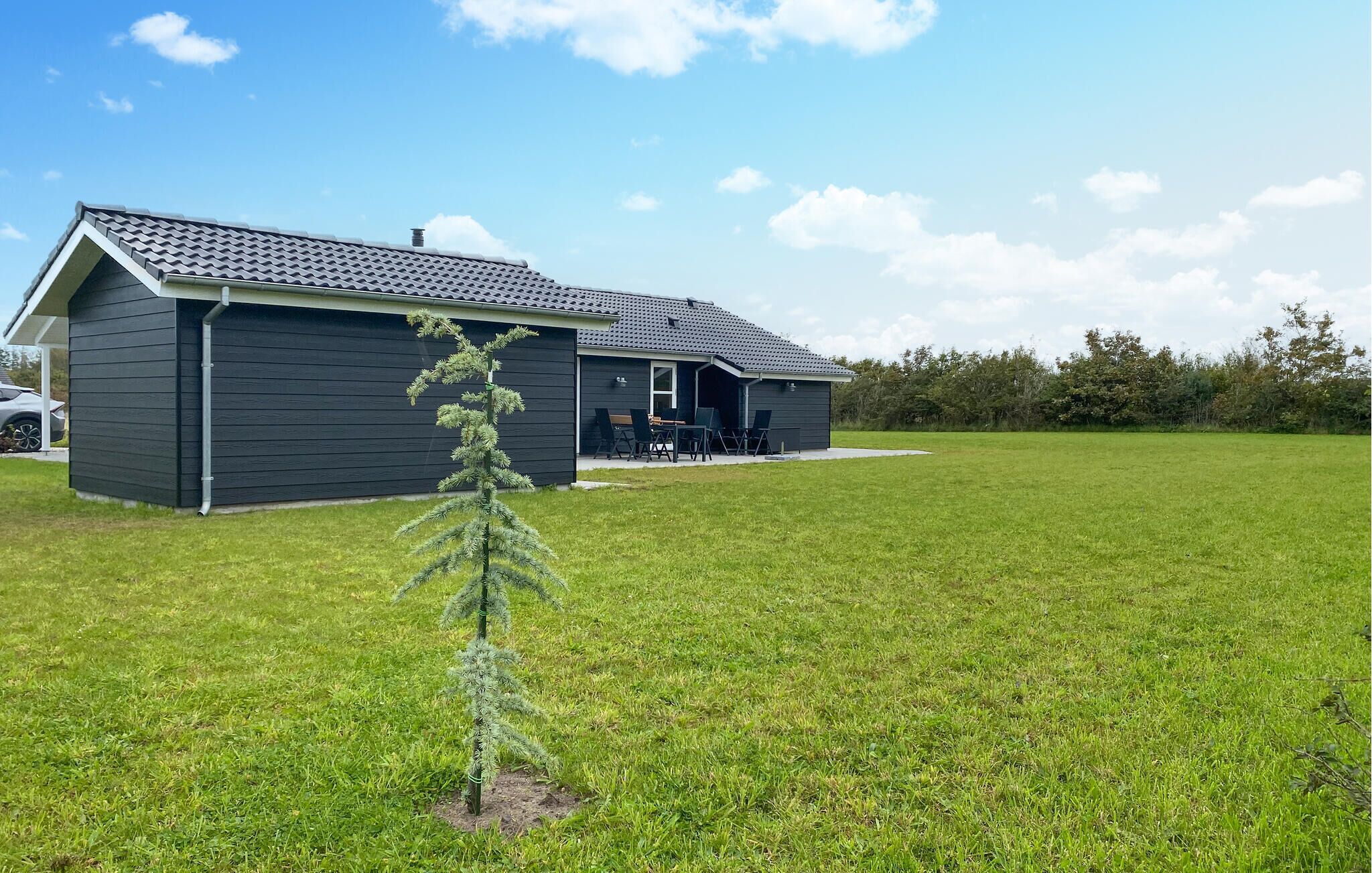 Een modern huis met een donkere gevel, een schuin dak en een klein voortoeltje met buitenmeubels.
