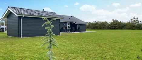 Een modern huis met een donkere gevel, een schuin dak en een klein voortoeltje met buitenmeubels.