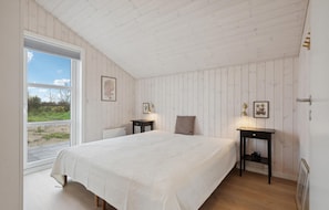 Relax in this serene bedroom with a large bed, two nightstands, and a window offering a view of a grassy field.
