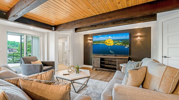 A modern living room with a large flat-screen TV, comfortable seating, and a view of a lake through large windows. - Amazing Lakefront Paradise with Perfect Location (Osage Beach)