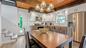 A modern kitchen with white cabinets, stainless steel appliances, and a wooden dining table. - Amazing Lakefront Paradise with Perfect Location (Osage Beach)