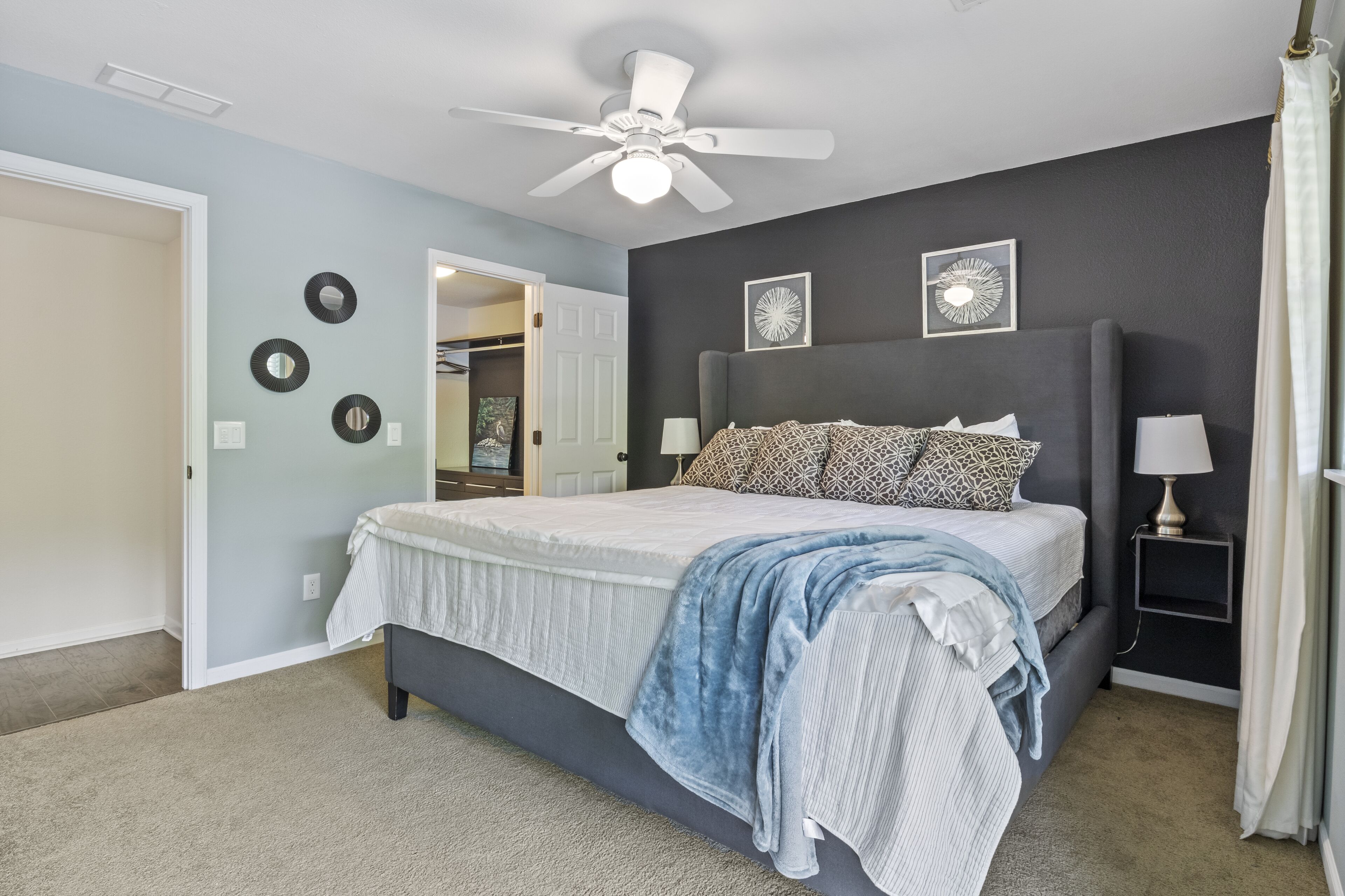 Un dormitorio con cama, ventilador de techo, decoración en la pared y mesita de noche.