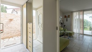 A modern interior with a sliding glass door leading to a stone wall outside, a glass table with a chair, and a treadmill in the background. - Beach front home in Sveti Ivan with WiFi (Sveti Ivan)