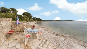 A stone patio with a table and chairs, a flag, and a view of the sea. - Beach front home in Sveti Ivan with WiFi (Sveti Ivan)