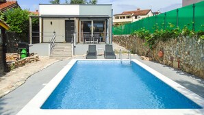 A rectangular swimming pool with a stone wall on one side and a green fence on the other. - Awesome home in Peroj (Peroj)