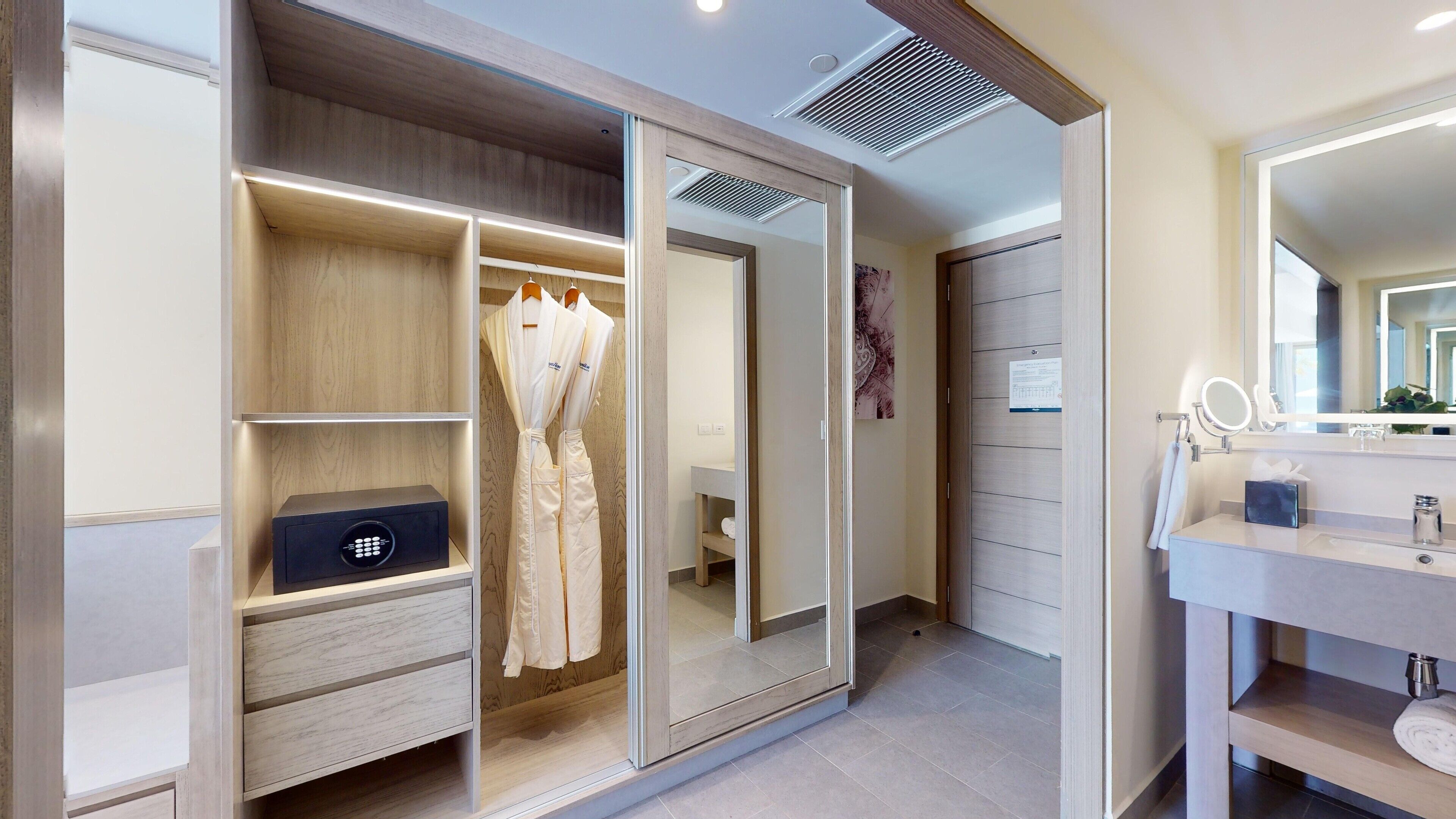 A modern bathroom with a vanity, mirror, and a walk-in closet with a built-in safe.