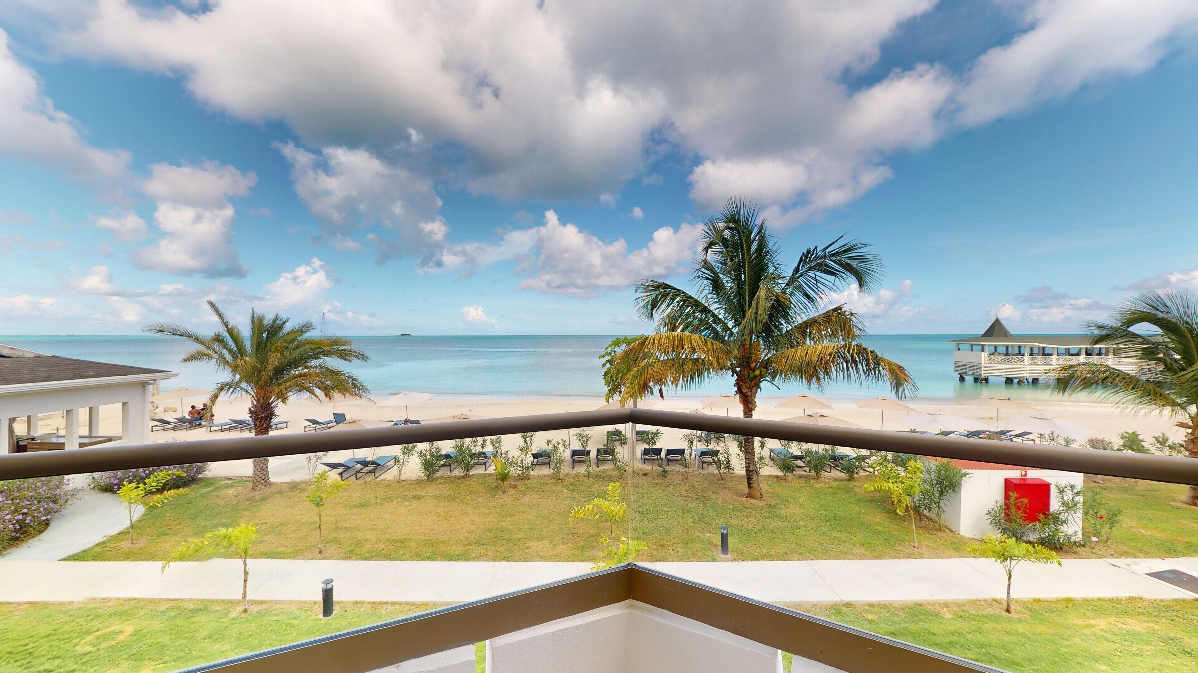 A balcony with a view of a beach, palm trees, and a pier.