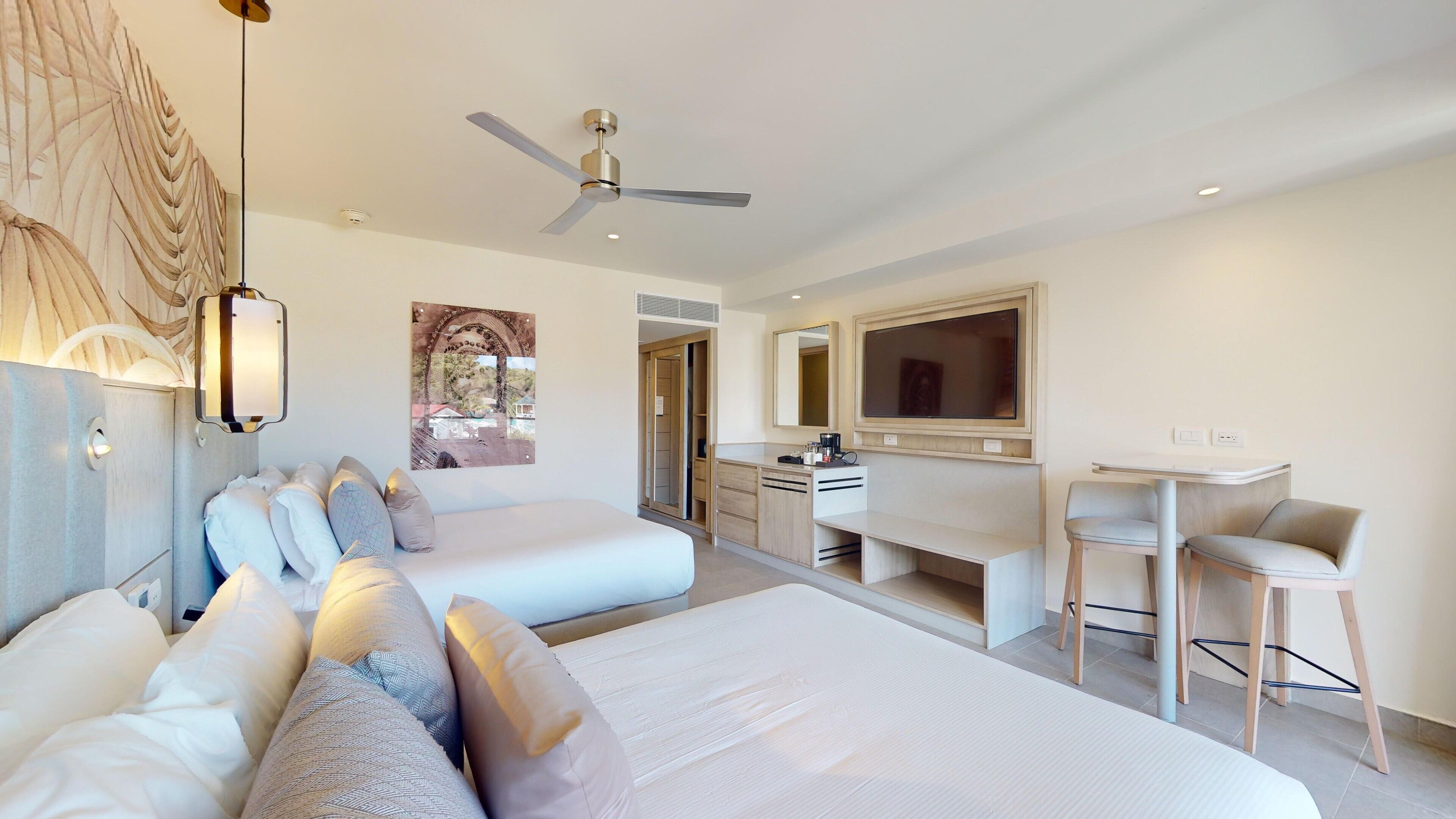 A modern hotel room with two beds, a desk, a chair, and a ceiling fan.