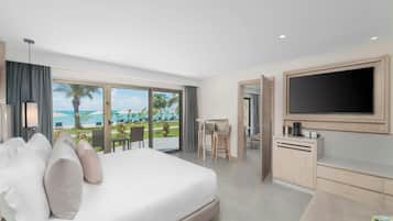A modern hotel room with a large bed, a TV, a desk, and a view of the beach.