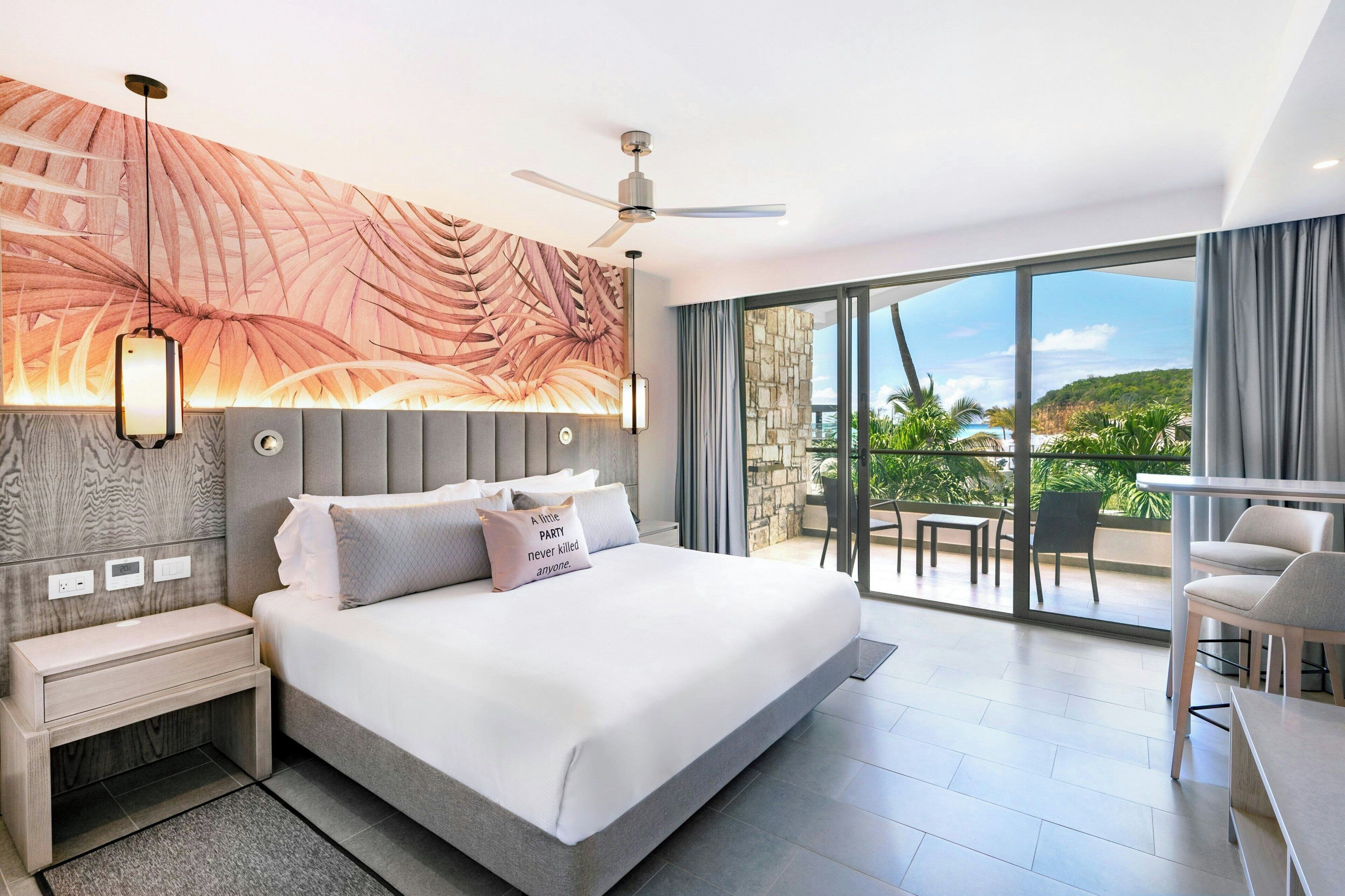 Une chambre d’hôtel moderne dotée d’un grand lit, d’un ventilateur de plafond, d’une vue sur l’extérieur et d’un balcon avec des sièges.