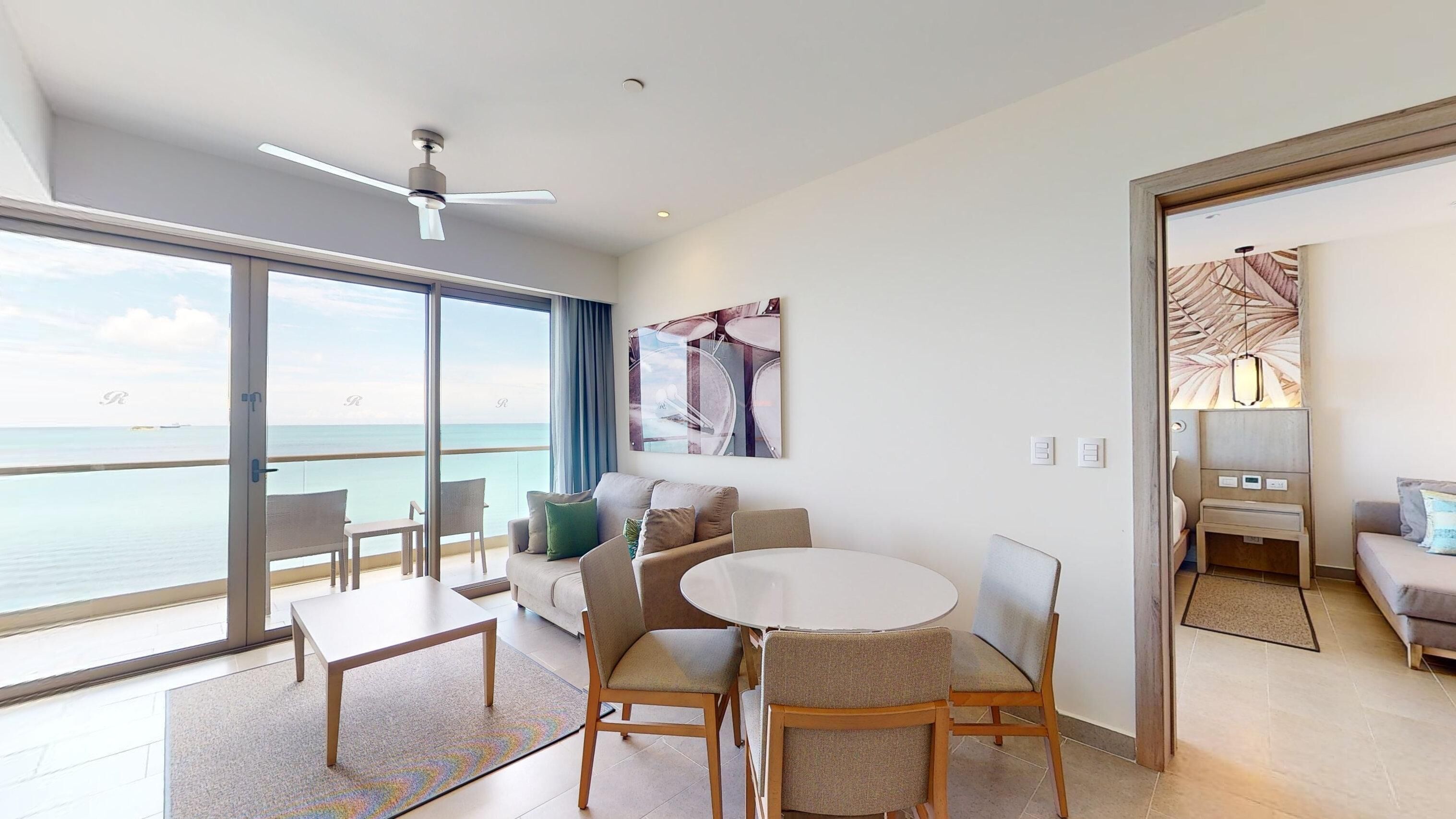 A modern hotel room with a balcony, a round dining table, and a sofa.