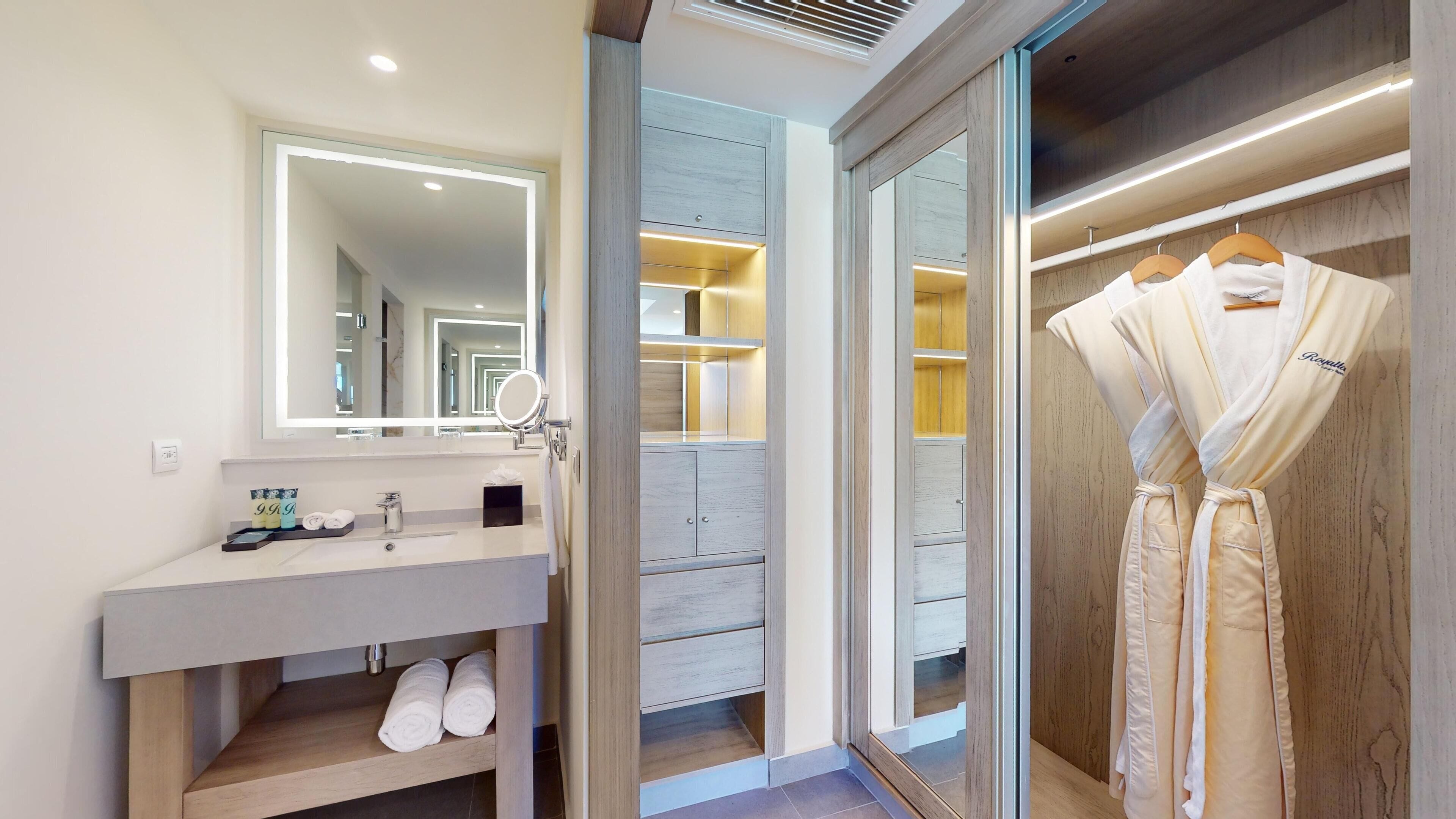 A modern bathroom with a vanity, a mirror, and a walk-in closet with wooden doors.