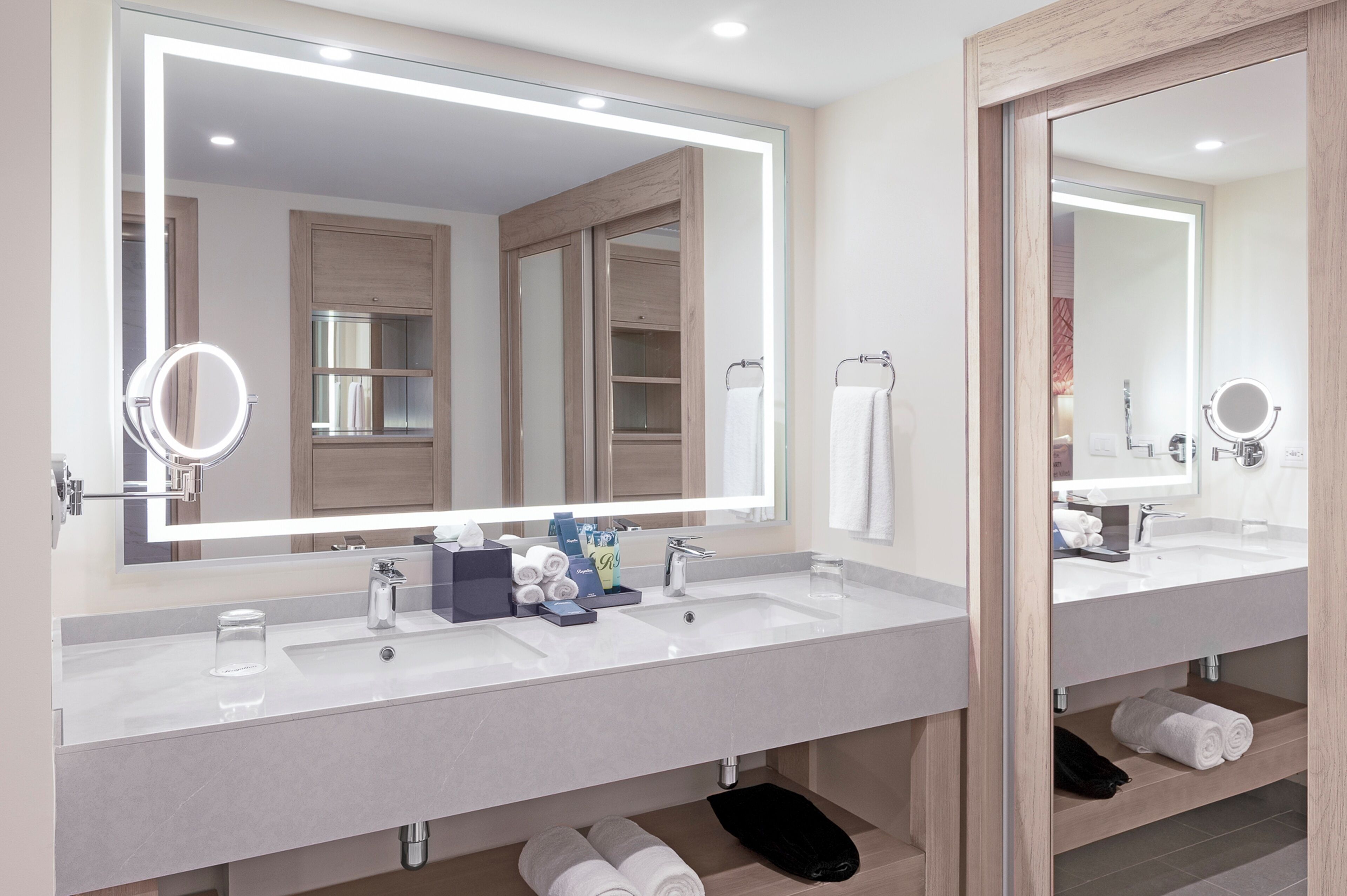 A modern bathroom with two sinks, a large mirror, and a vanity with storage.