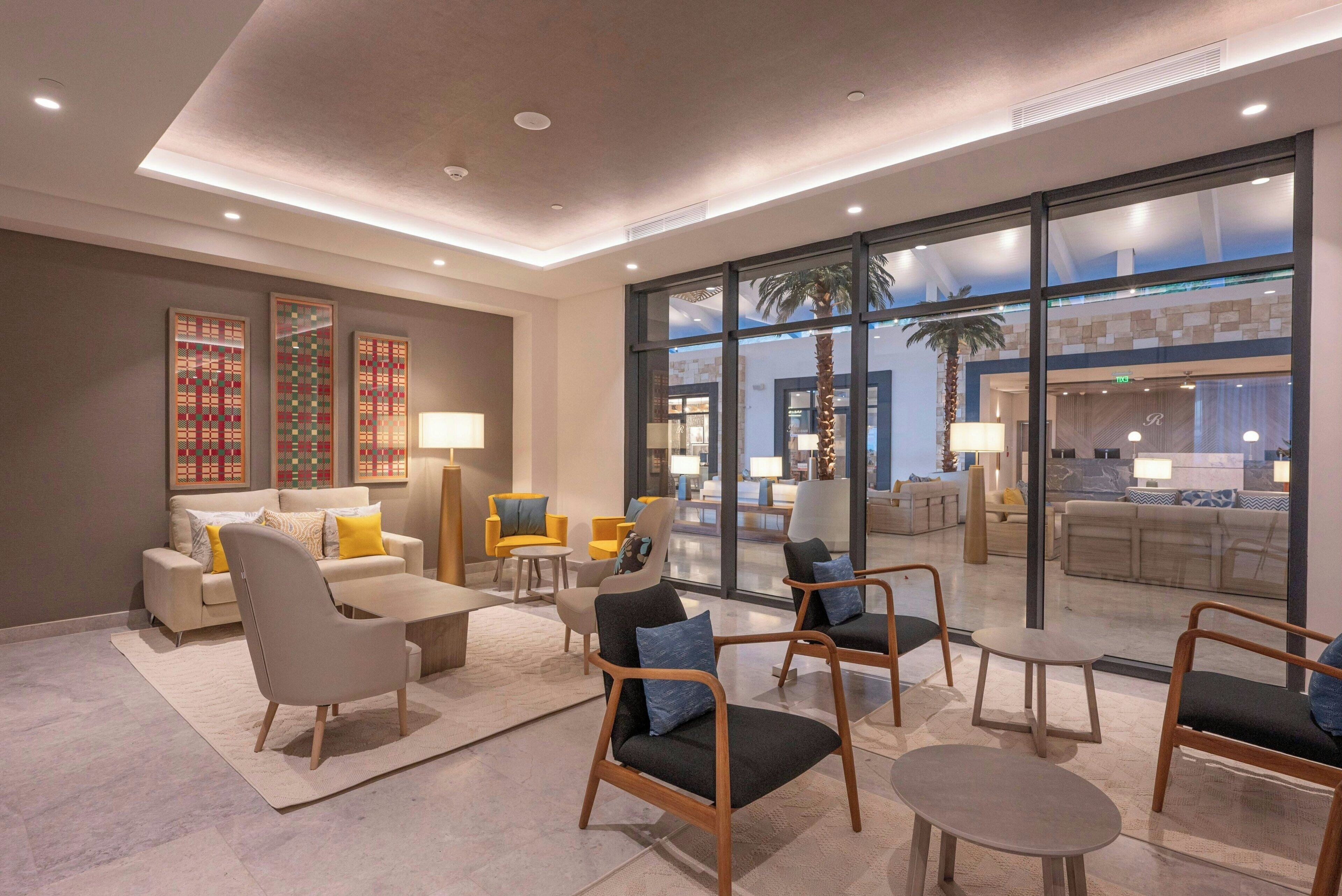 Een moderne hotel lobby met een zithoek, grote ramen en uitzicht op het interieur van het hotel.