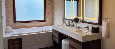 A modern bathroom with a large bathtub, two sinks, a vanity with drawers, a large mirror, and a window providing natural light.