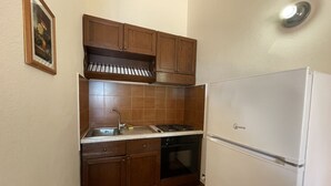 A compact kitchen with wooden cabinets, a white refrigerator, a stove, and a sink.