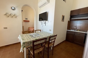 A compact kitchen with a dining area, a mounted TV, and a tiled backsplash. - Collina sul Golfo 17 Apartment (Mola)