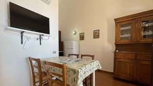 A dining area with a table, chairs, a television mounted on the wall, a refrigerator, and wooden cabinets.