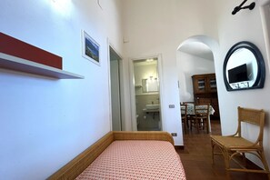 A bedroom with a bed, a red shelf, a mirror, and a dining area with chairs and a table. - Collina sul Golfo 17 Apartment (Mola)