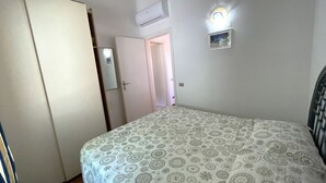 A bedroom with a bed, a wardrobe, a door, an air conditioning unit, and a wall-mounted light fixture.