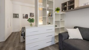 A modern living room with a grey sofa, white shelving units, and a white cabinet with drawers. - ARCHIMEDE, 53 · Apt 3 - Monolocale con spazio esterno (Milano)