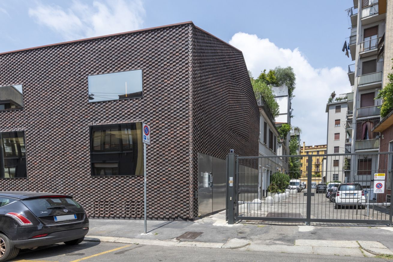 Een modern gebouw met een geruit gevel, een hekpoort en een geparkeerde auto.