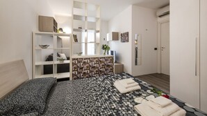 A modern bedroom with a bed, a white console table, a patterned rug, and a small plant. - ARCHIMEDE, 53 · Apt 3 - Monolocale con spazio esterno (Milano)