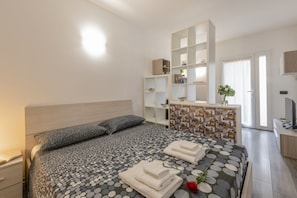 A bedroom with a bed, a bedside table, a dresser, a mirror, and a TV. - ARCHIMEDE, 53 · Apt 3 - Monolocale con spazio esterno (Milano)