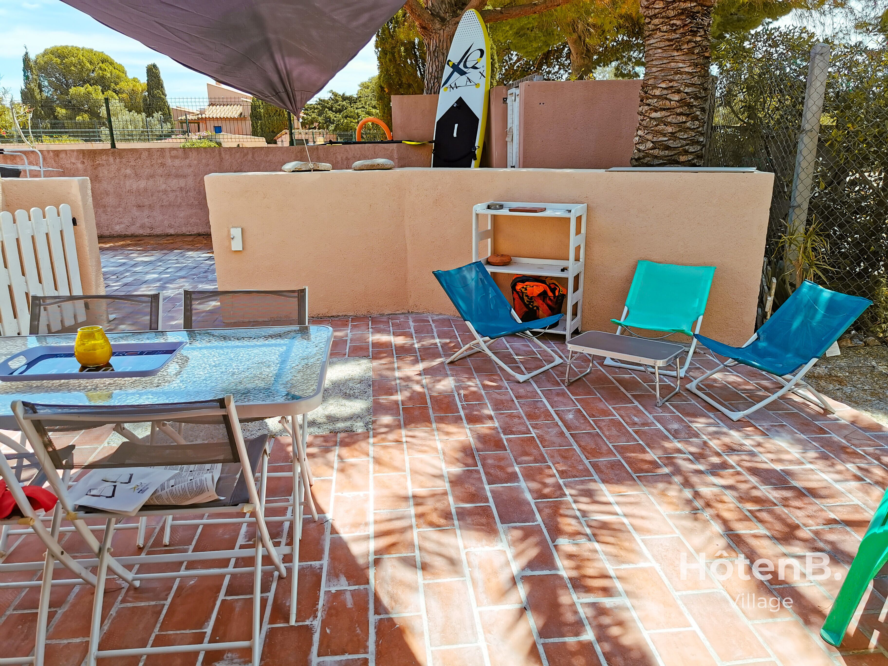 A patio area with a glass table, two blue lounge chairs, a yellow vase, and a white chair.
