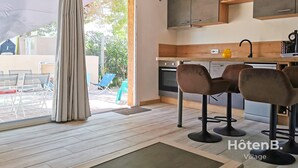 A modern kitchen with wooden cabinets, a sink, and bar stools. - Natural Escape: Air-Conditioned T2 BIS, Pools, and Private Estate in Fitou! (Fitou)