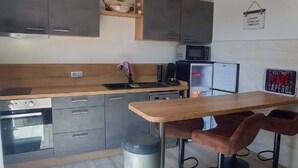 A compact kitchen with a wooden countertop, stainless steel appliances, and a small dining area with stools. - Natural Escape: Air-Conditioned T2 BIS, Pools, and Private Estate in Fitou! (Fitou)