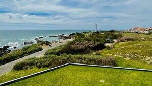 A coastal landscape with a lighthouse, grassy areas, and a paved path leading to the sea.