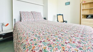 A bedroom with a bed, a chair, a lamp, and a wooden shelf.