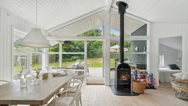 Una habitación amplia con una gran mesa de madera, sillas blancas, una chimenea y ventanas grandes que ofrecen vistas al exterior.