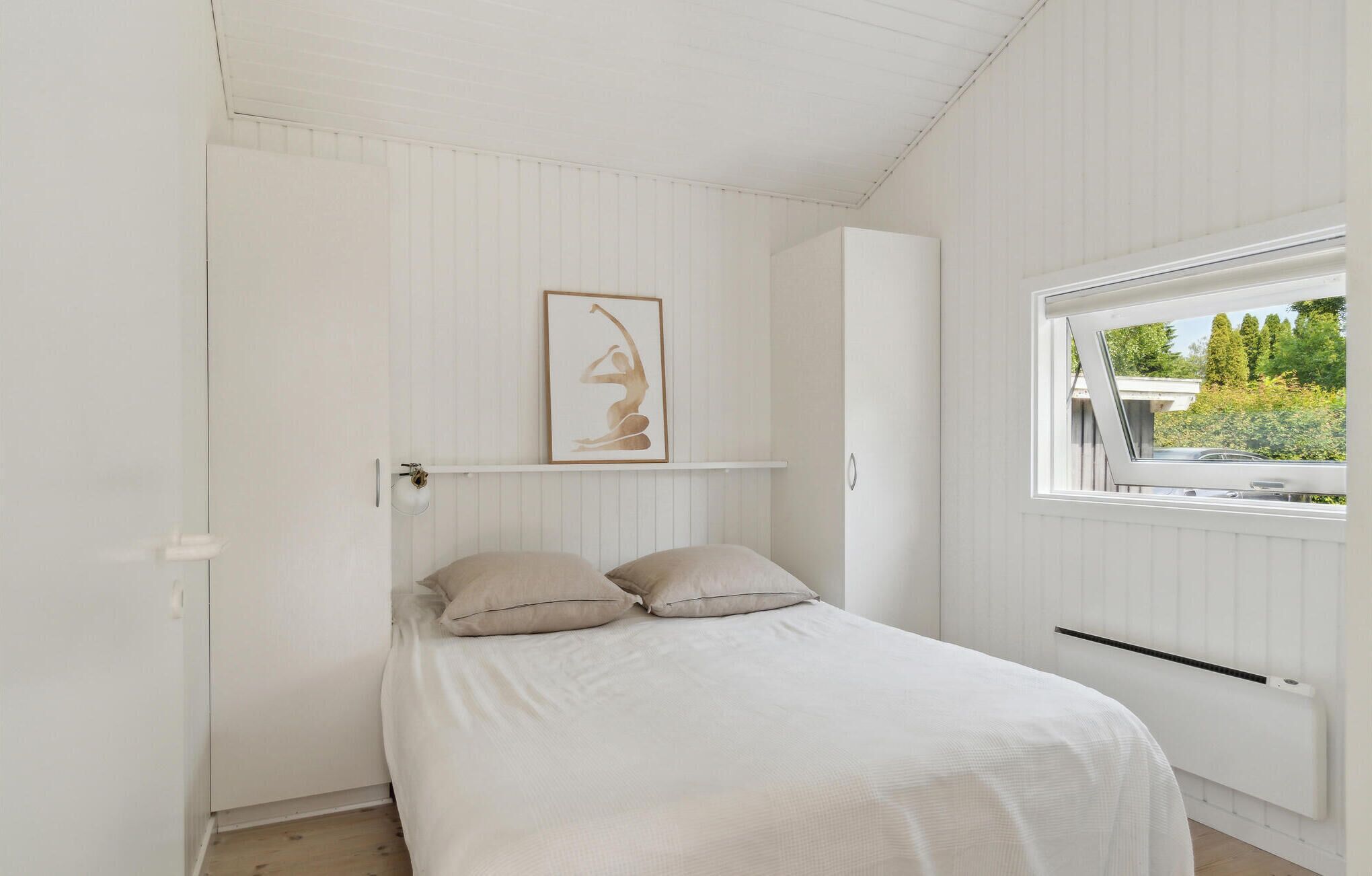 A bedroom with a bed, a window, and a wall-mounted shelf with a framed picture.