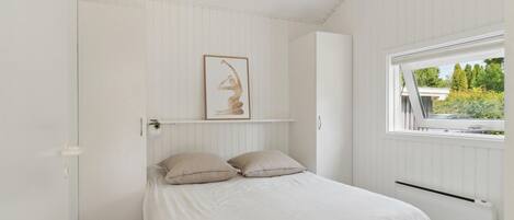 A bedroom with a bed, a window, and a wall-mounted shelf with a framed picture.