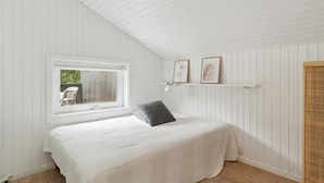 Un dormitorio con cama, ventana y estante con fotografías enmarcadas.