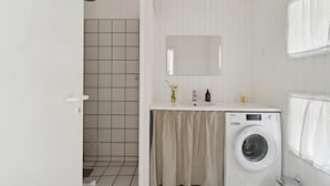 Un baño pequeño con ducha, lavabo y lavadora.