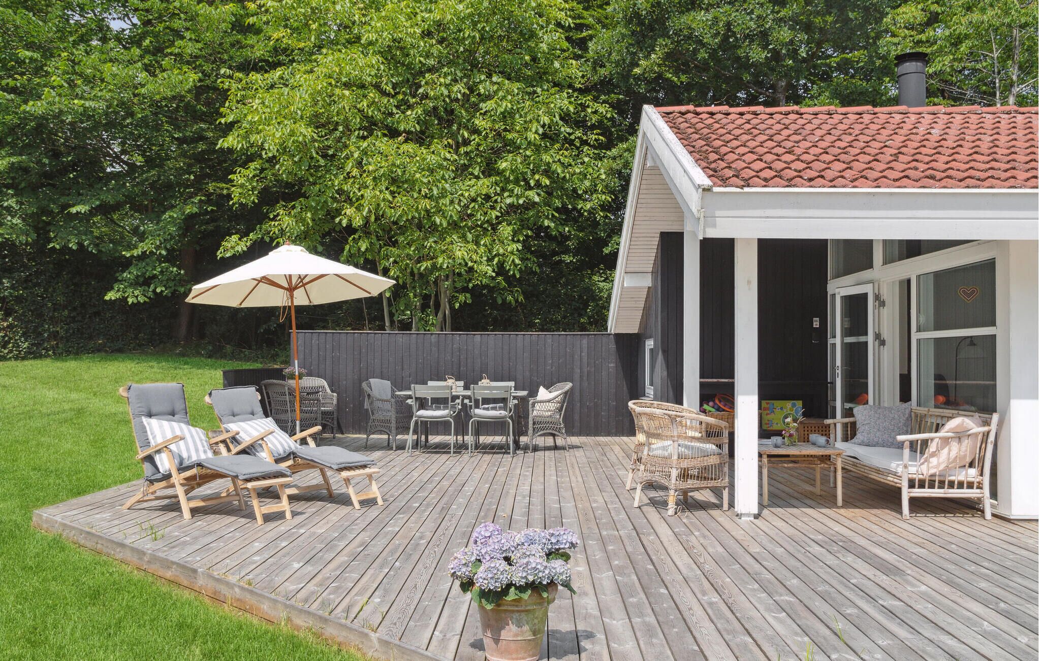 A wooden deck with outdoor furniture, a covered seating area, and a house with a tiled roof.