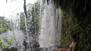 Eine Person sitzt an einem Wasserfall in einer natürlichen Umgebung.