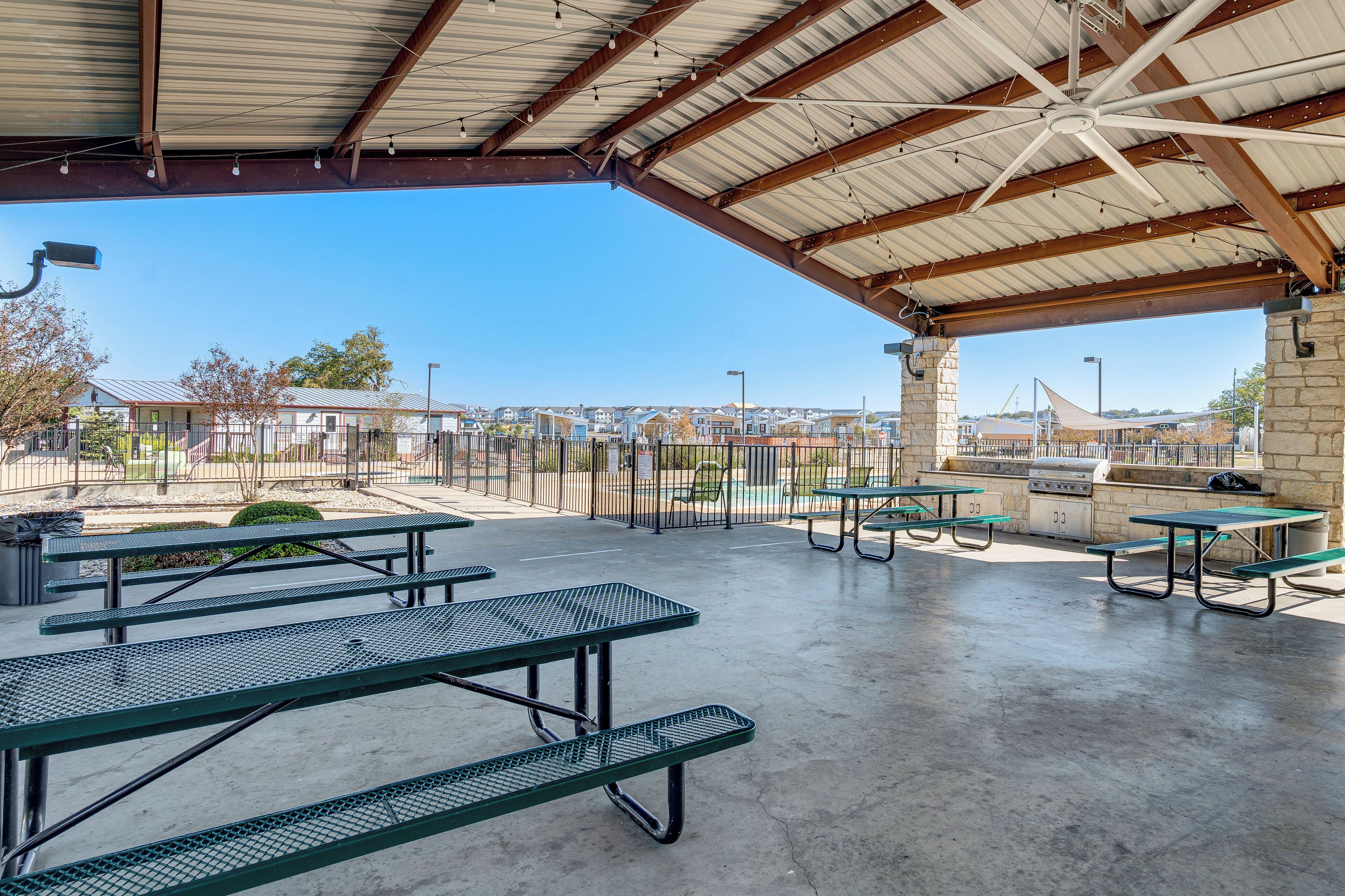 An outdoor covered picnic area with picnic tables and a barbecue grill.