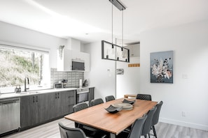 A modern kitchen with grey cabinets, a wooden dining table, and a hanging light fixture.