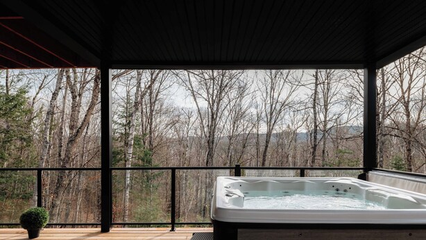 Un bain à remous sur une terrasse en bois, avec vue sur une zone boisée.