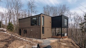 Une maison moderne à deux étages, dotée de grandes fenêtres, d’une terrasse et d’un espace salon extérieur.