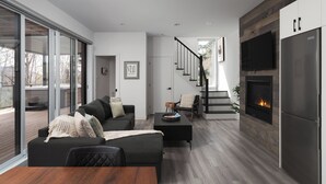 Un salon moderne avec un canapé, une table basse et une cheminée. Un escalier mène à un balcon.