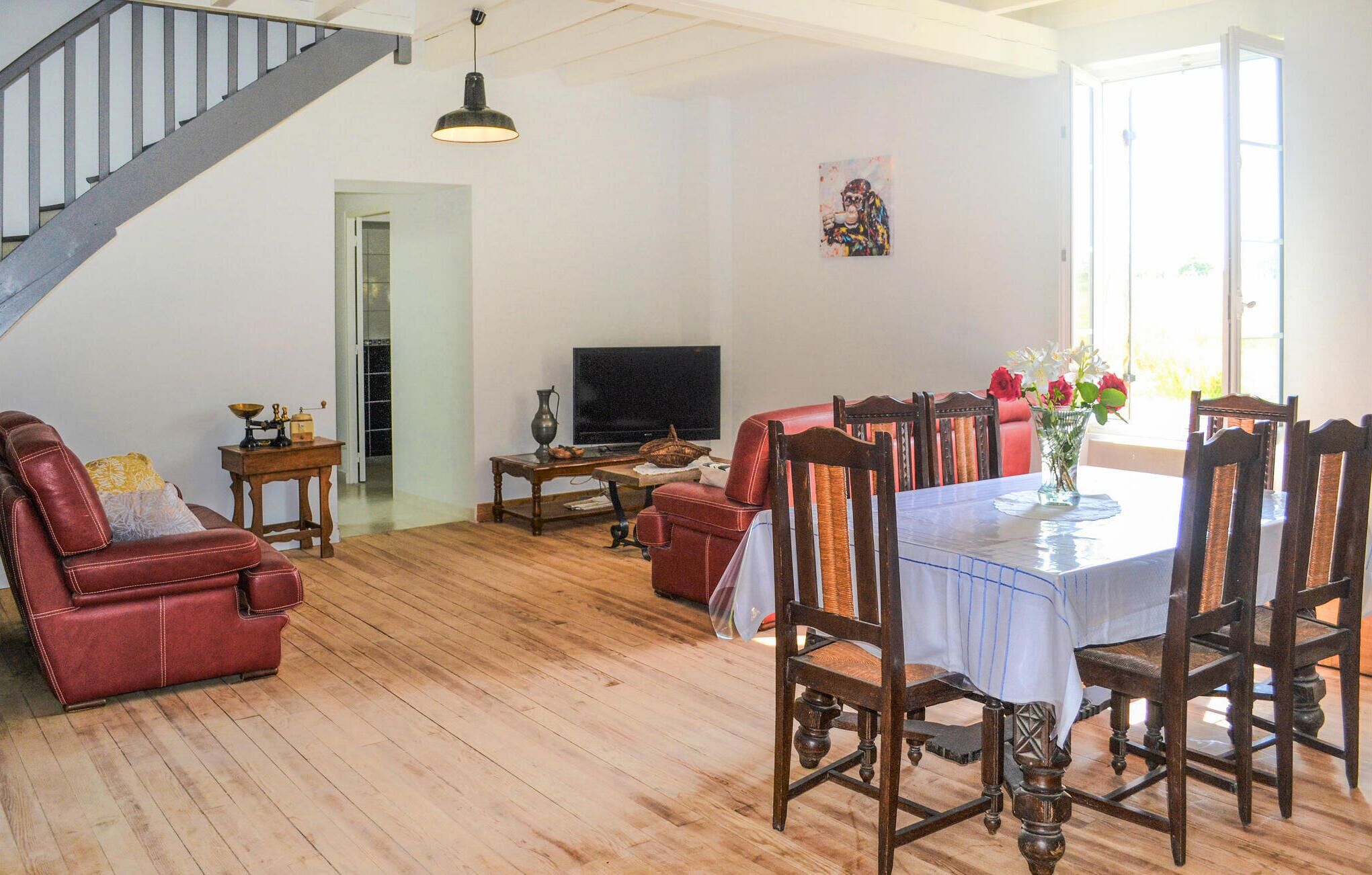 A spacious living room with a wooden floor, a red leather sofa, a dining table with chairs, a television, and a painting on the wall.