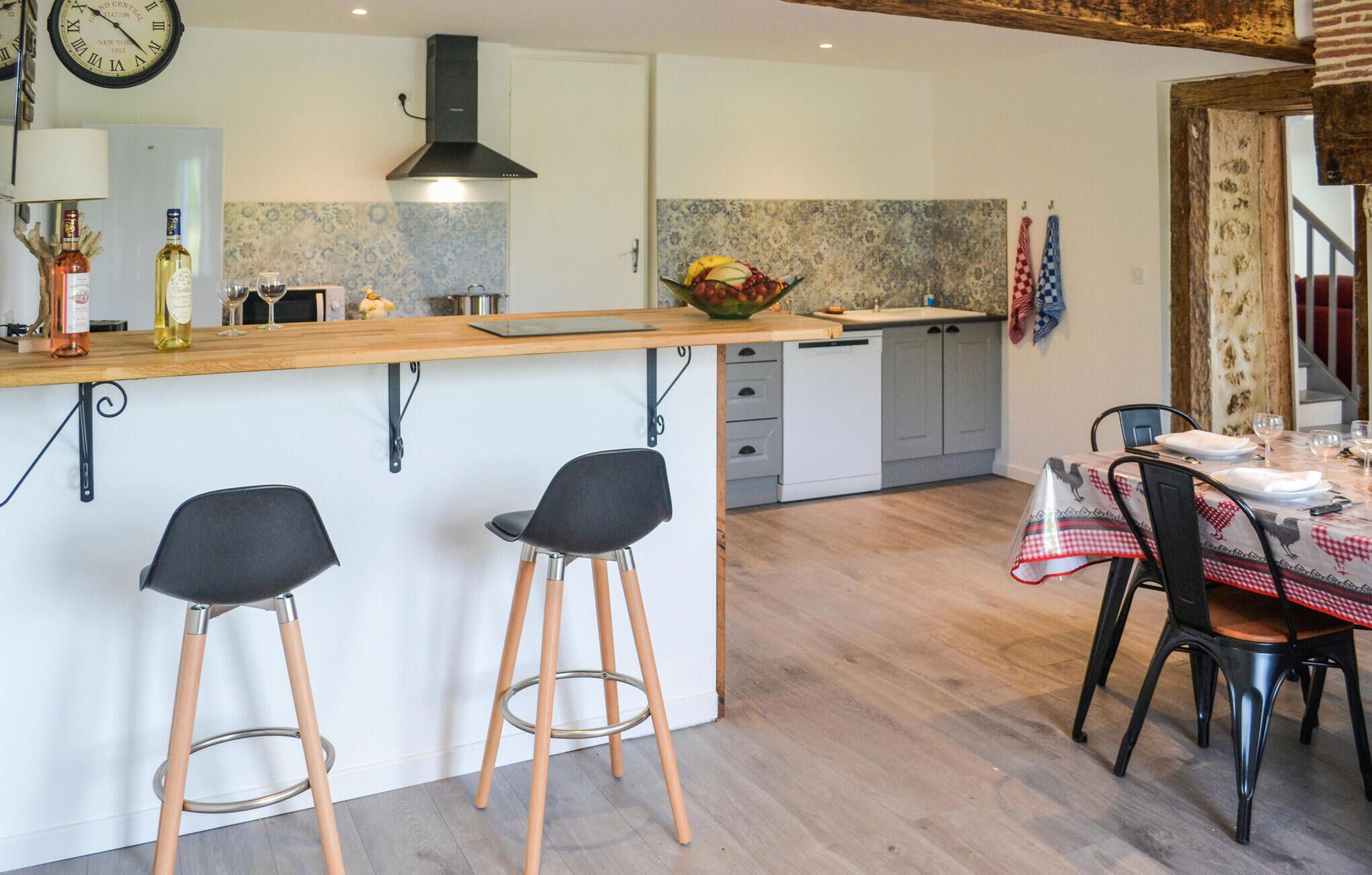 Una cocina moderna con una isla central, taburetes de bar y un comedor con una mesa preparada para dos.