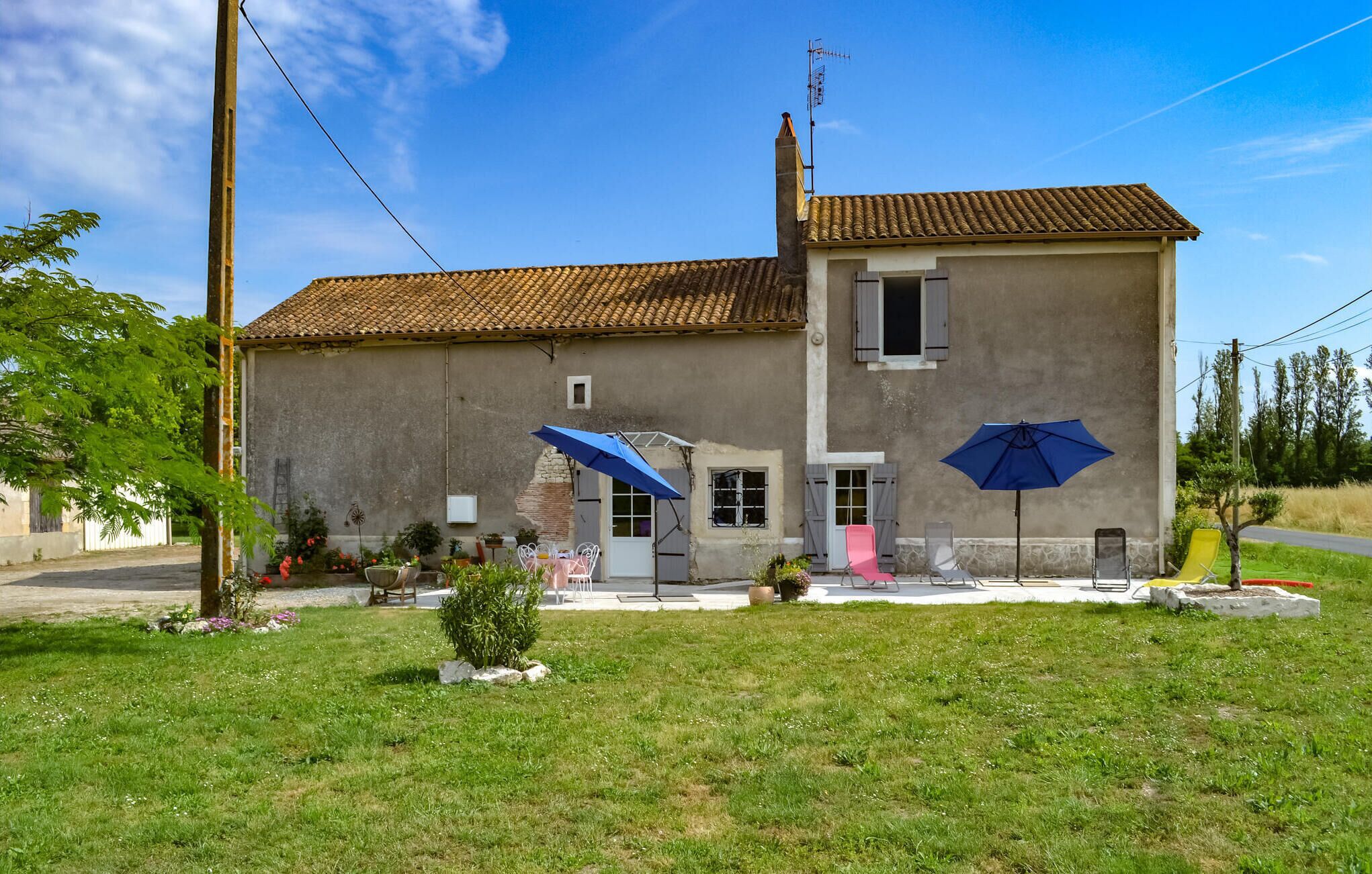 A two-story house with a tiled roof, a chimney, and a small garden with outdoor furniture.